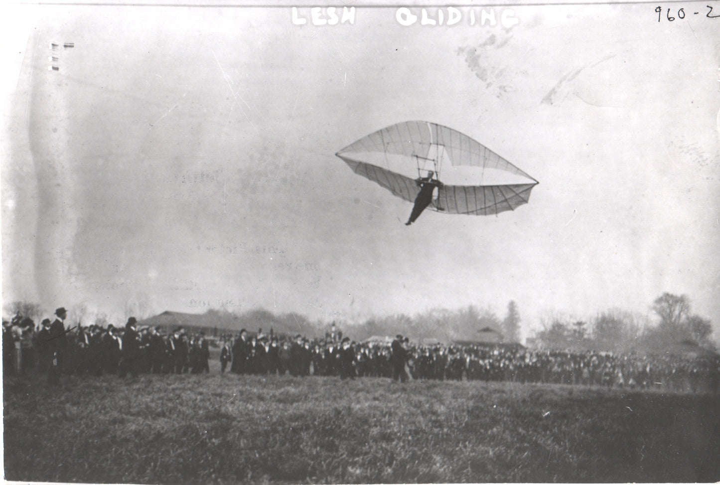 Vintage photo of a glider in flight with a large crowd watching.