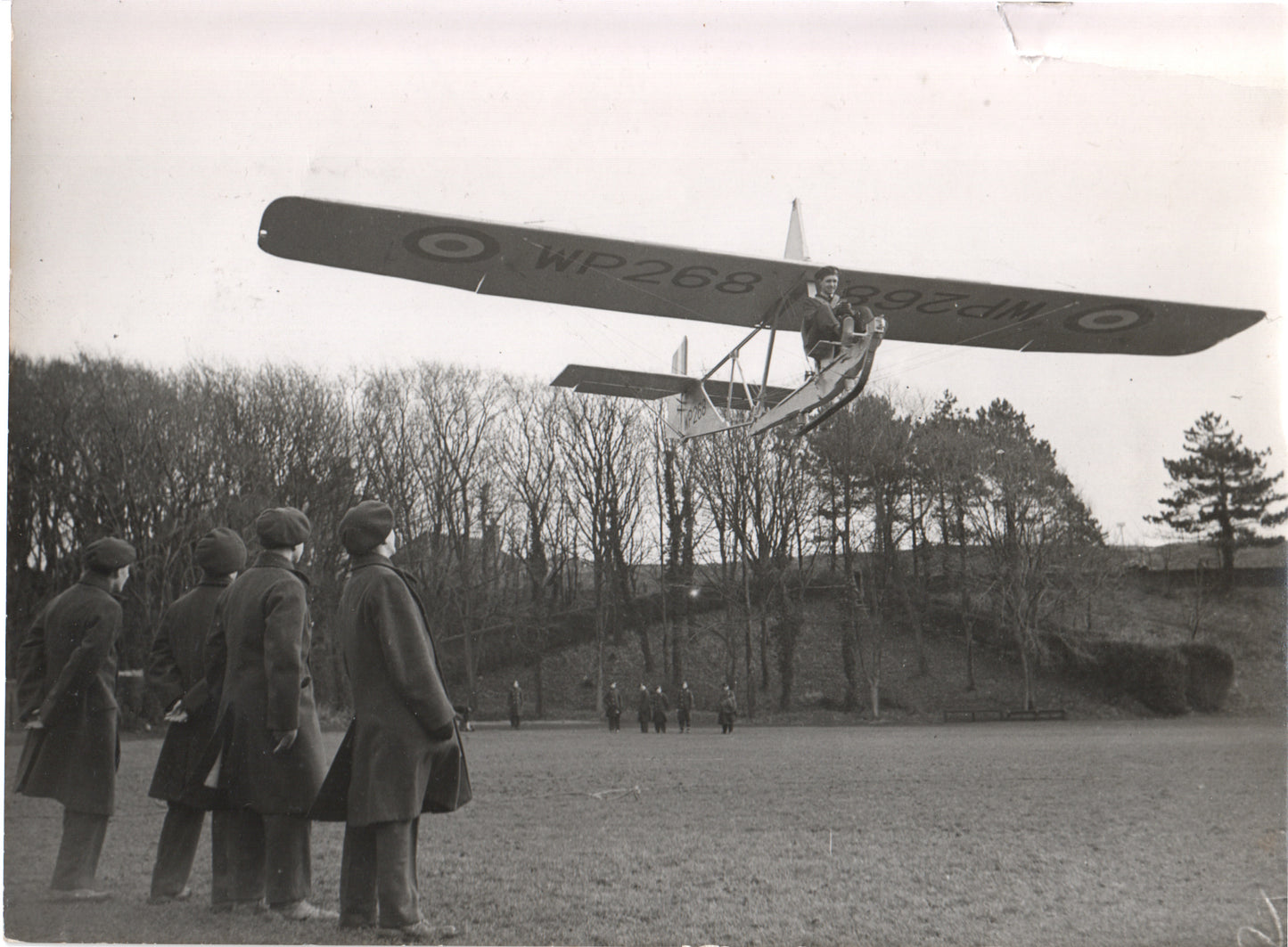 A vintage photograph of a WWII-era British training aircraft flying above a group of observers. - Image: Folder27-17