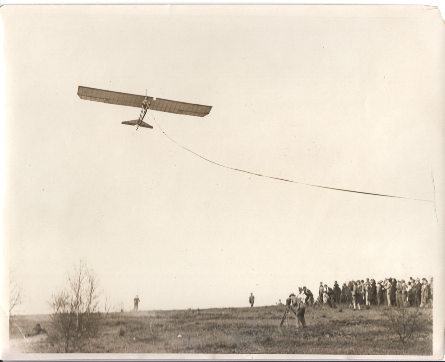 Black-and-white photograph of a vintage aircraft in flight over a crowd on a hillside. - Image: Folder22-8