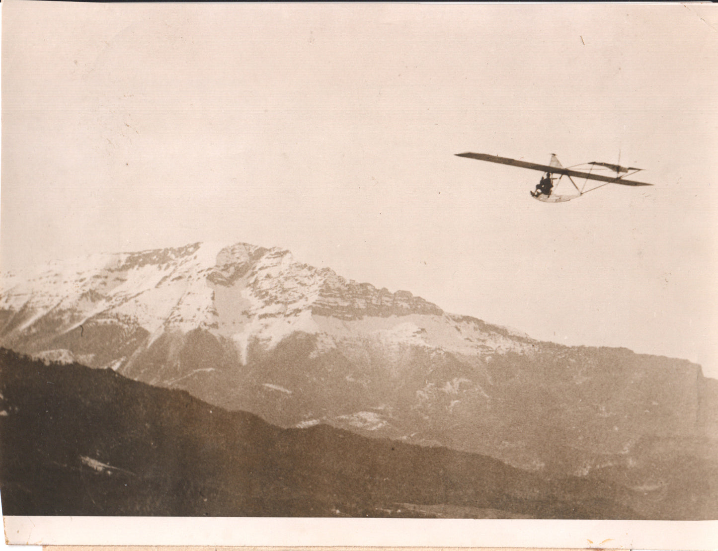Vintage black and white photo of a glider flying over snowy mountains