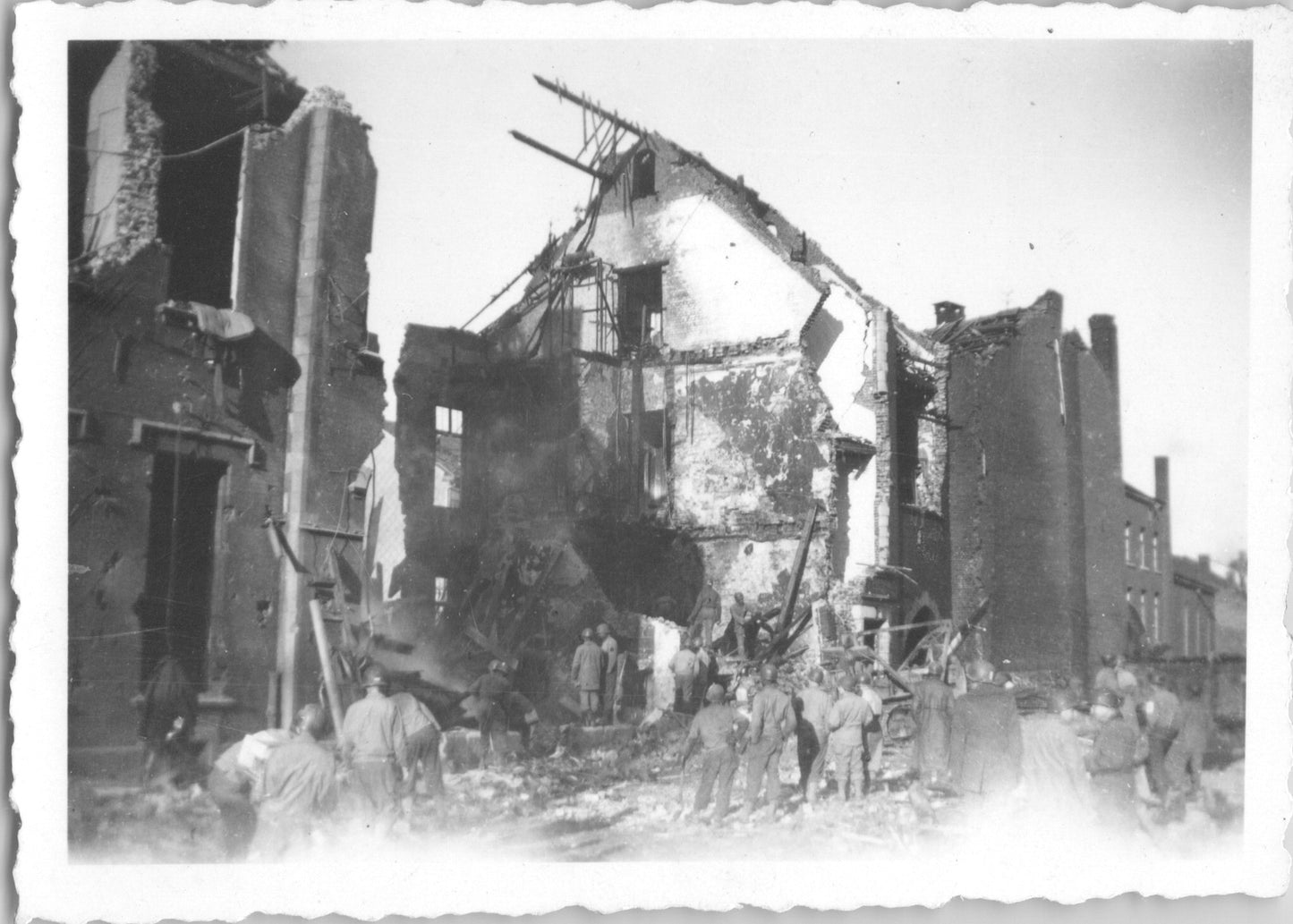 A black and white photograph depicting a bombed building and people surveying the destruction. - Image: 2025-08-25-0022