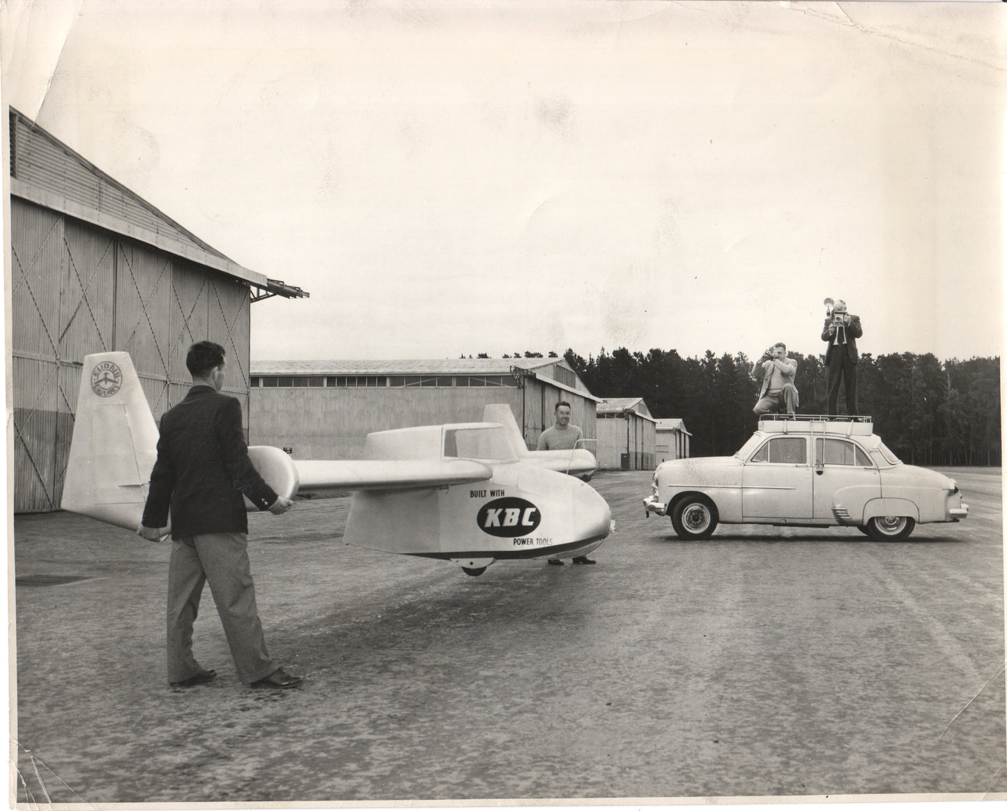 A vintage photo featuring an experimental aircraft and a classic car with models posing on top. - Image: Folder25-11