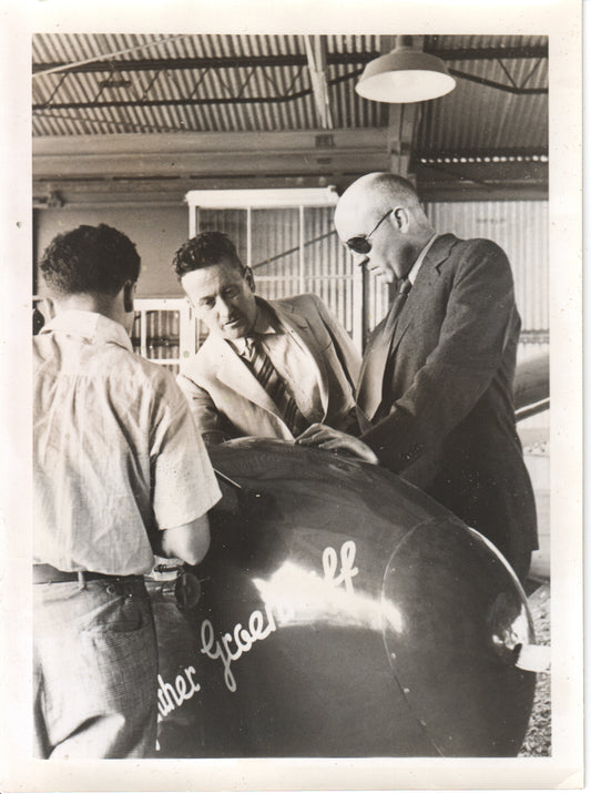 Black and white photo of three men inspecting an aircraft model in a hangar setting - Image: Folder23-10