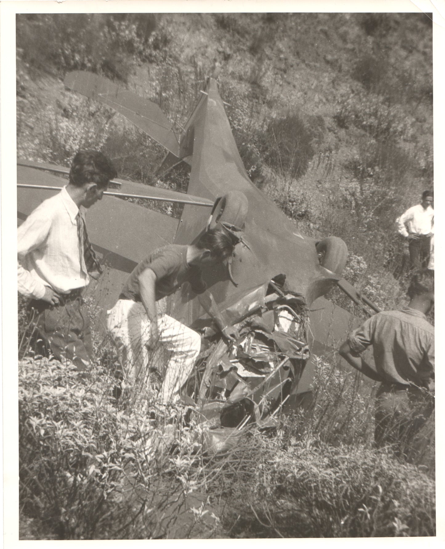 Vintage photograph of a group of men examining a crashed aircraft in a natural setting. - Image: Folder18-8