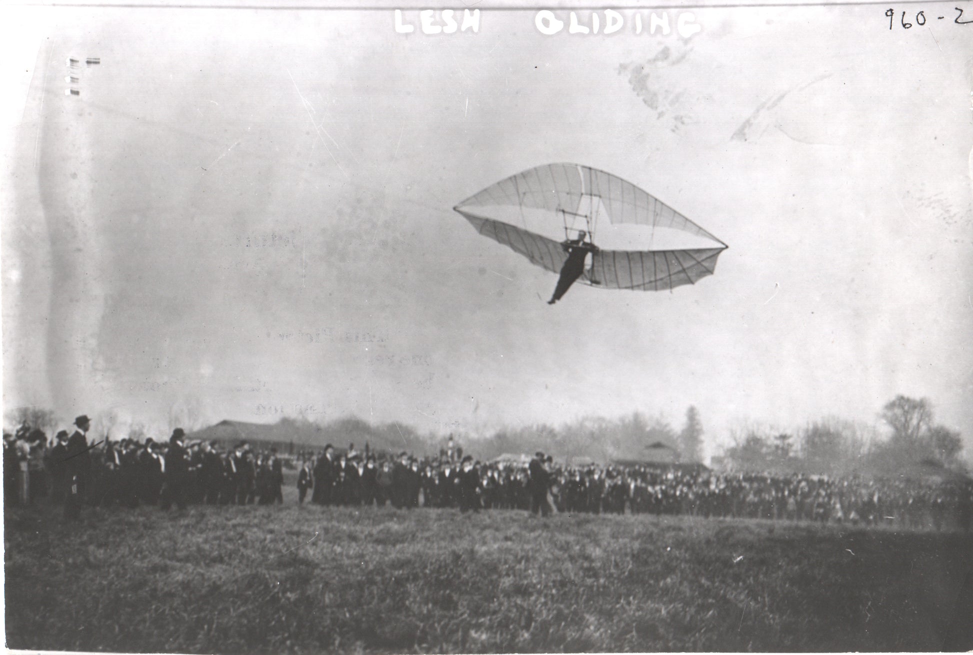 Vintage photo of a glider in flight with a large crowd watching.