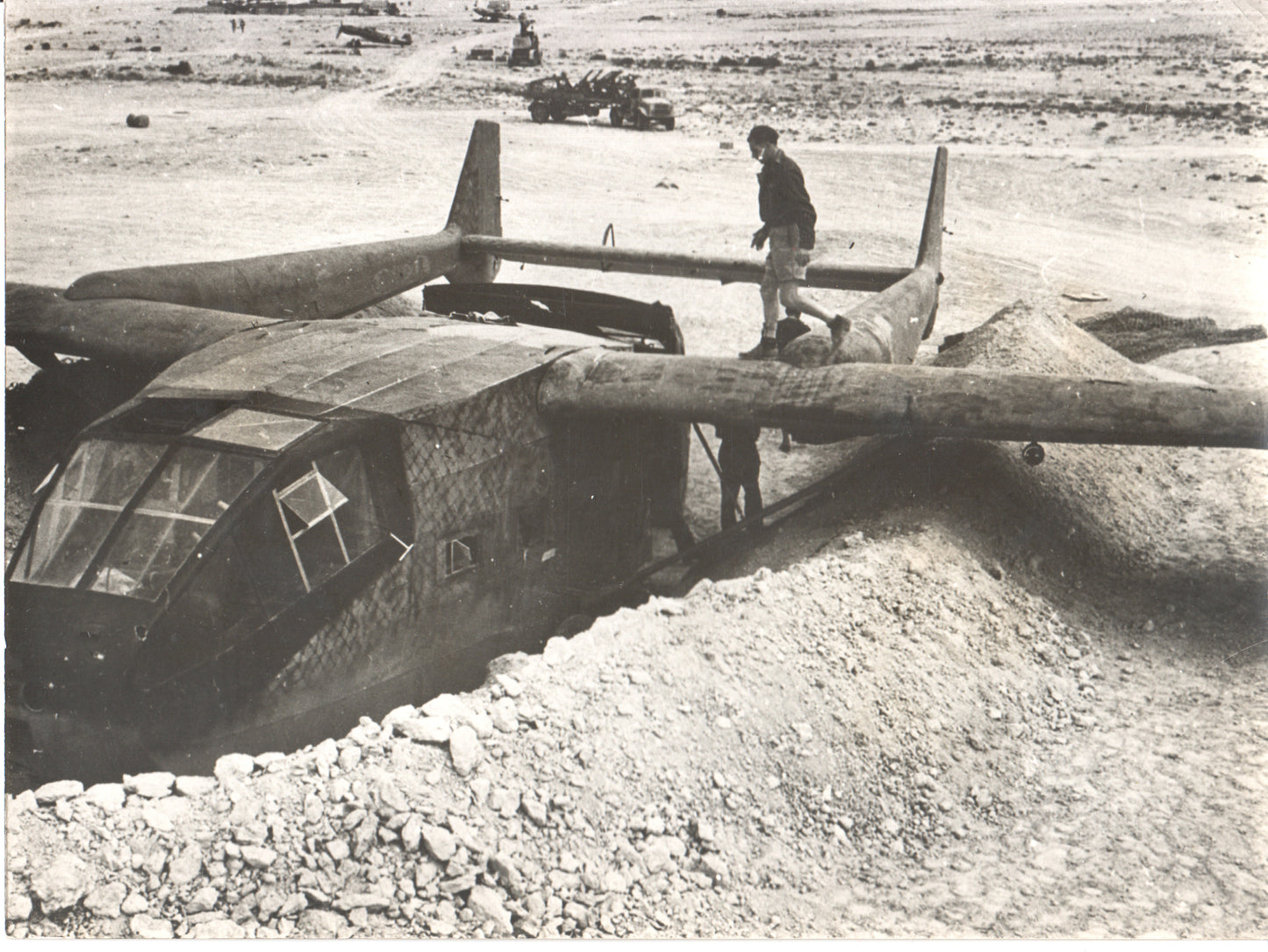 A vintage black-and-white photograph of a military aircraft in a desert setting. - Image: Folder24-11