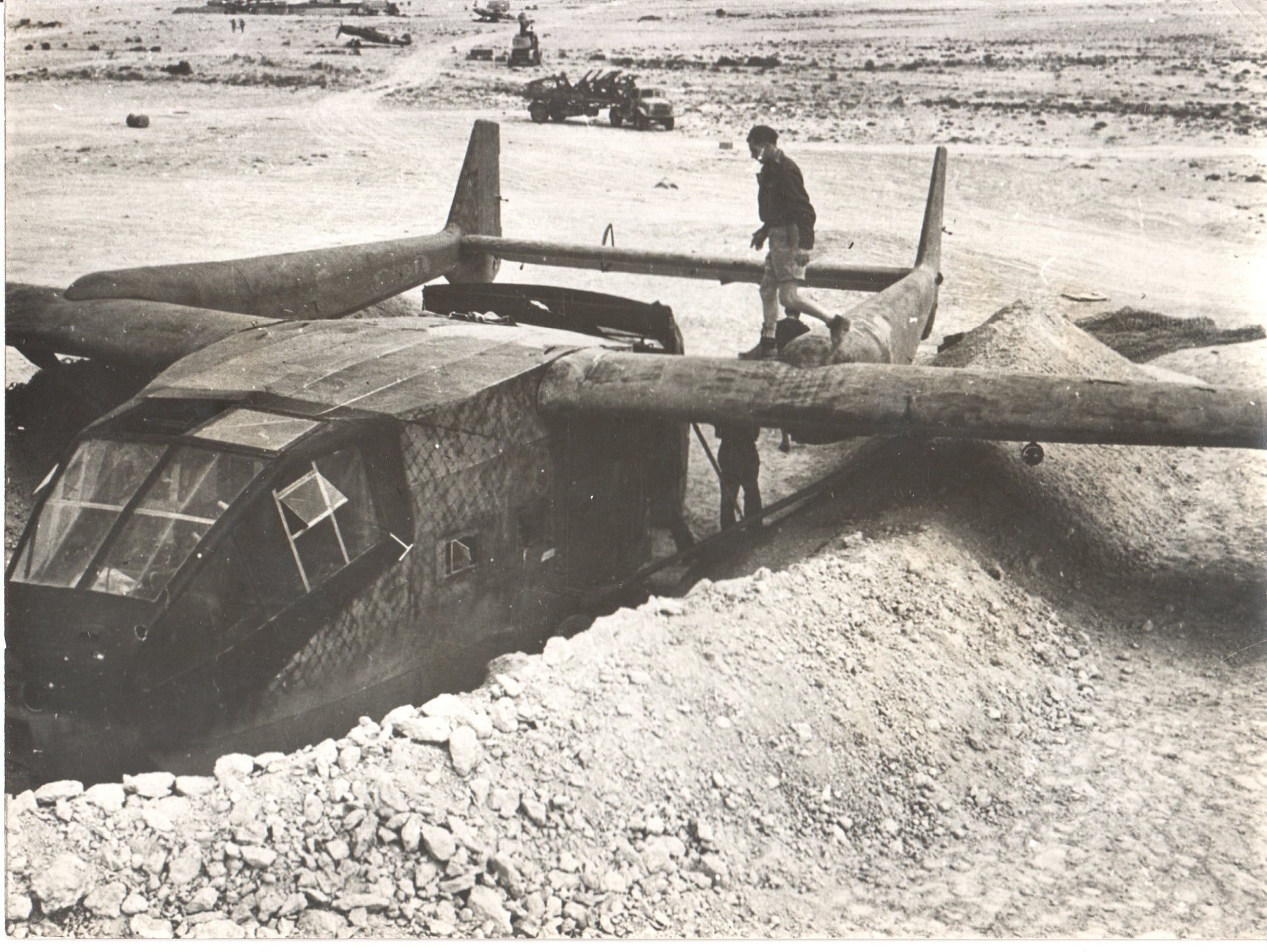 A vintage black-and-white photograph of a military aircraft in a desert setting. - Image: Folder24-11