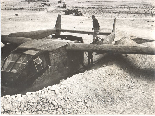 A vintage black-and-white photograph of a military aircraft in a desert setting. - Image: Folder24-11