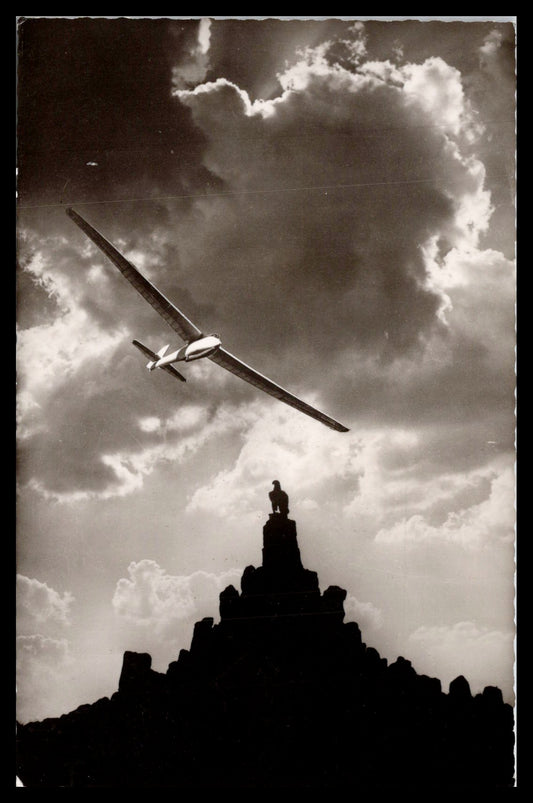 Black and white photo of a glider flying above an eagle statue on a rocky pedestal. - Image: MA-PC_0033