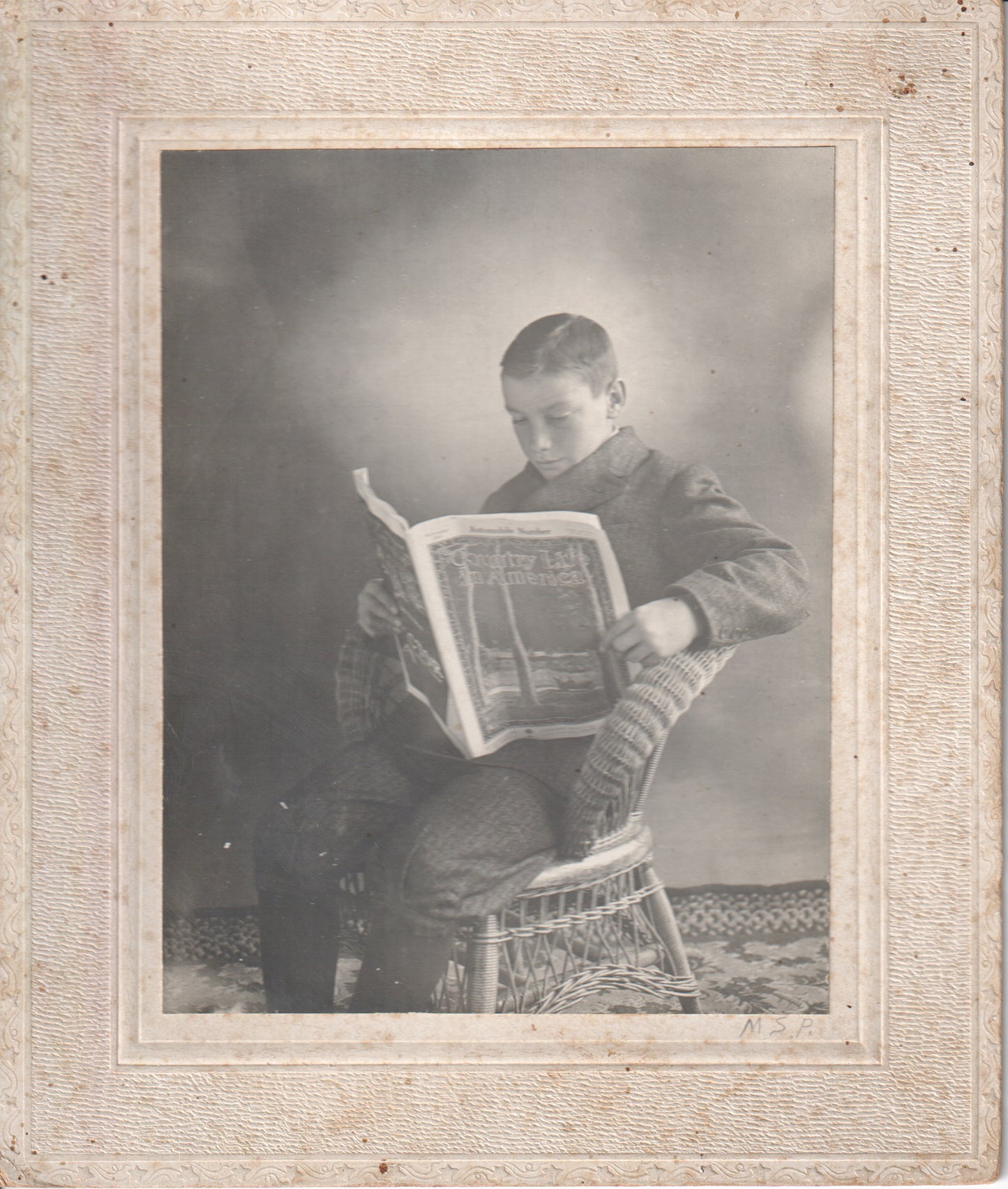 Black and white photograph of a young boy sitting in a chair, reading a magazine. - Image: 2025-04-13-0060