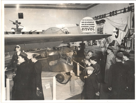 A vintage black and white photograph of a crowded aviation exhibition featuring an airplane and attendees in period attire. - Image: Folder26-7