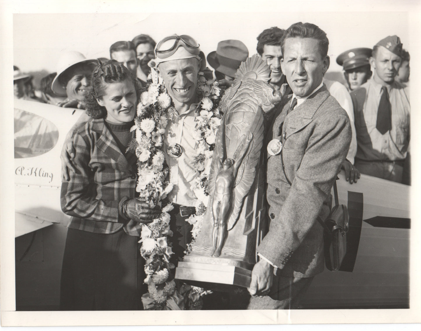 Vintage photograph of a smiling aviator celebrating with a trophy and floral garlands. - Image: Folder13-4