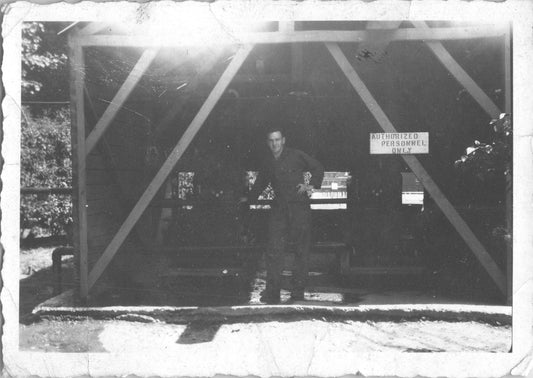 A vintage black and white photo of a man in uniform in front of a building with a sign. - Image: 2025-08-25-0027