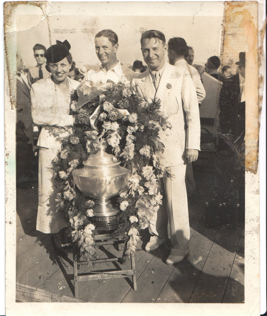 Vintage photo of three individuals posing with a trophy and flowers. - Image: Folder24-5