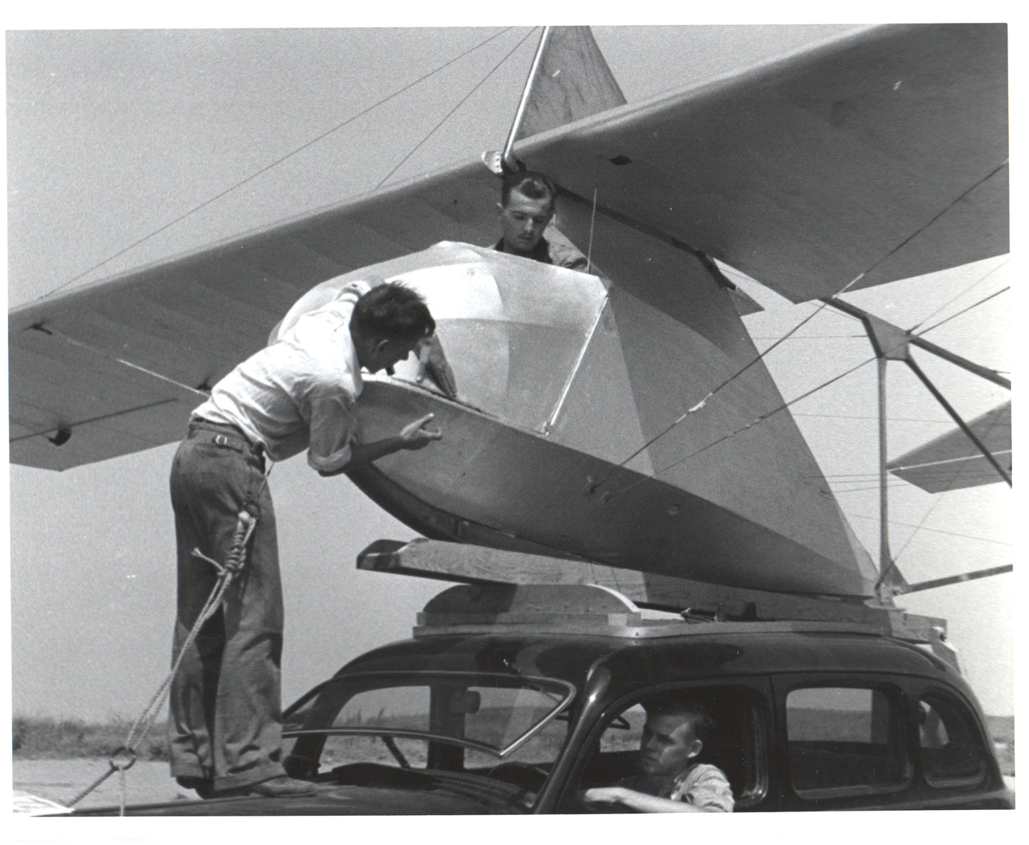 Two men assembling an aircraft on top of a car in a vintage black and white photo. - Image: Folder16-9
