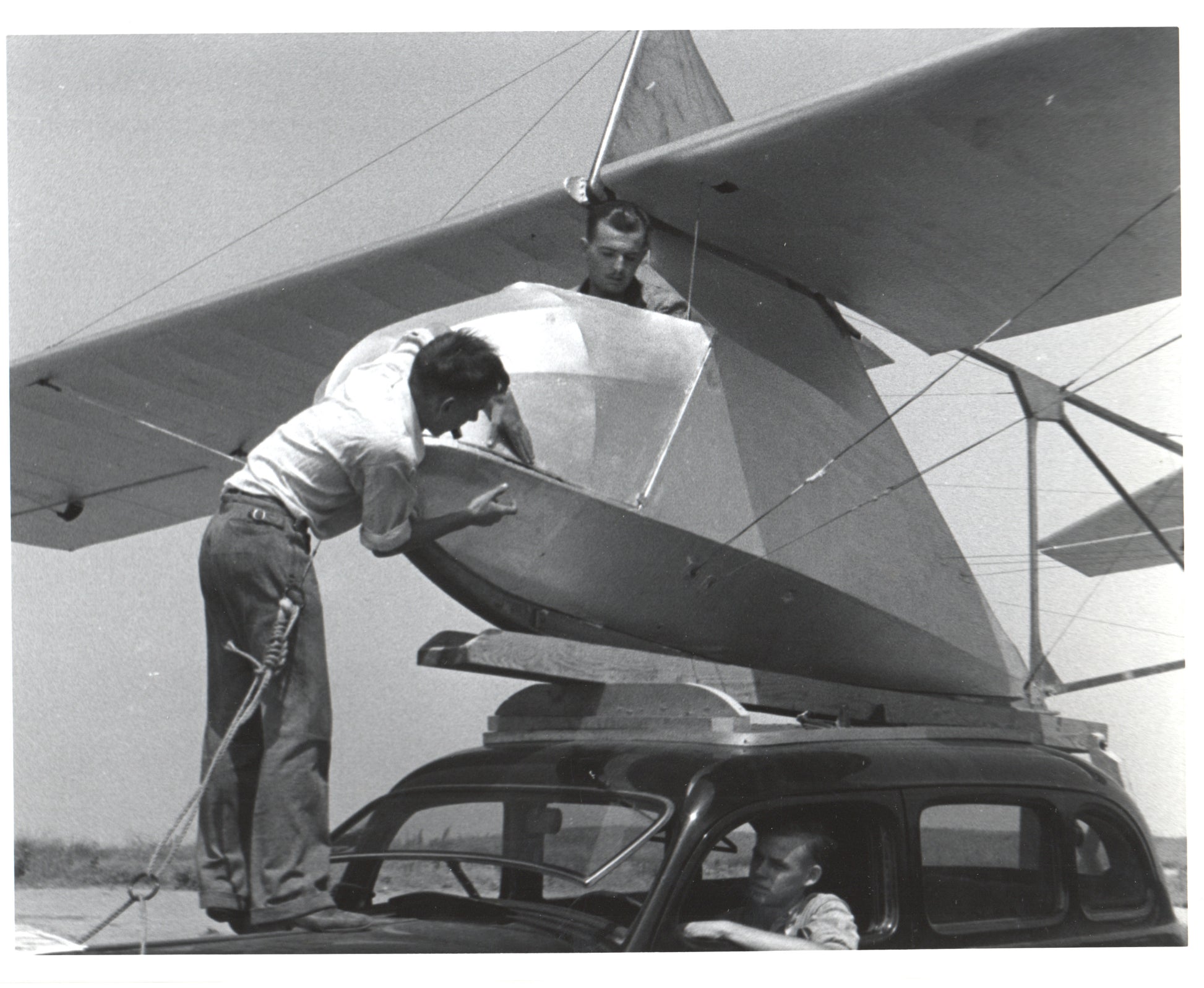 Two men assembling an aircraft on top of a car in a vintage black and white photo. - Image: Folder16-9