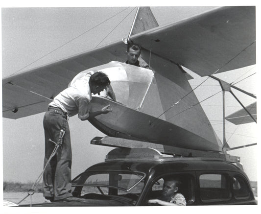 Two men assembling an aircraft on top of a car in a vintage black and white photo. - Image: Folder16-9