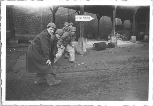 A group of five WWII soldiers posing playfully near an air raid shelter sign. - Image: 2025-08-25-0003