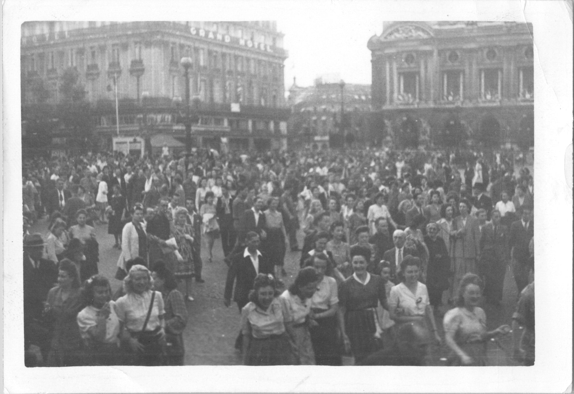 Black and white photograph of a large crowd in a public square with a grand hotel in the background. - Image: 2025-08-25-0078