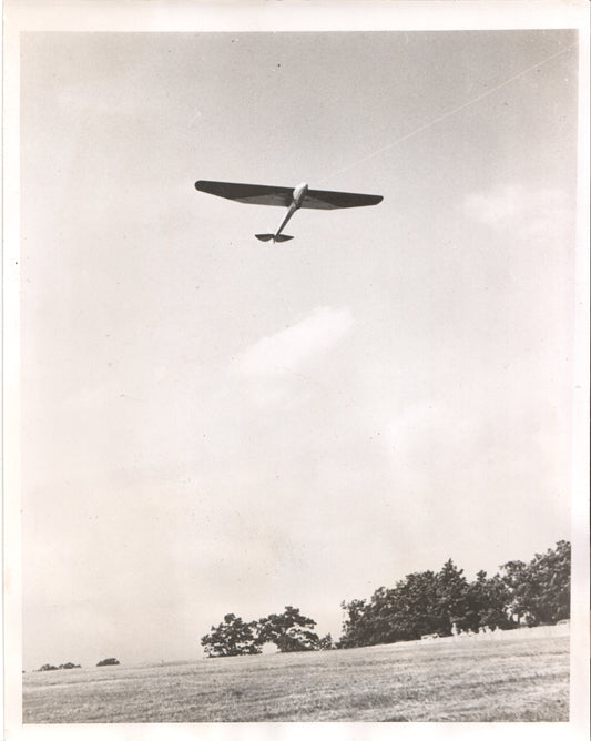 Black and white photograph of a glider flying above a grassy field. - Image: Folder19-16