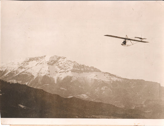 Vintage black and white photo of a glider flying over snowy mountains