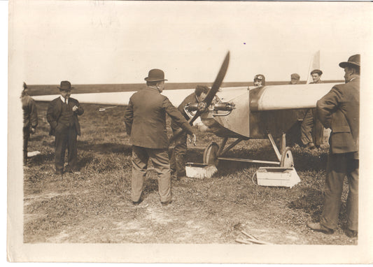 A historical photograph depicting men inspecting a vintage aircraft on a grassy field. - Image: Folder28-17