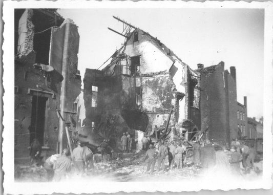 A black and white photograph depicting a bombed building and people surveying the destruction. - Image: 2025-08-25-0022