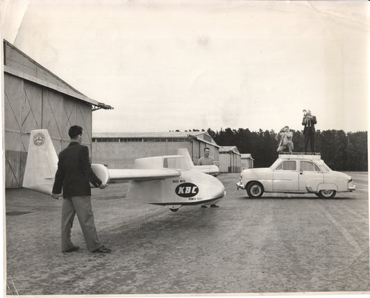 A vintage photo featuring an experimental aircraft and a classic car with models posing on top. - Image: Folder25-11
