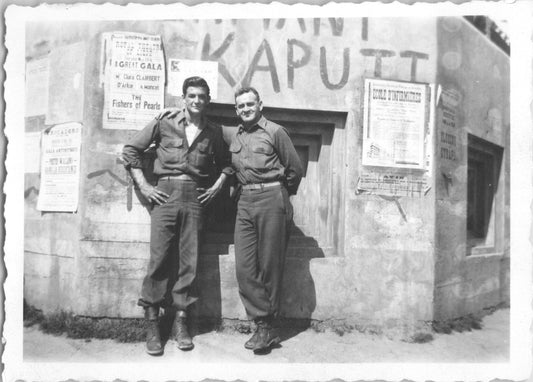 Two soldiers pose in front of a wall covered with posters and graffiti. - Image: 2025-08-25-0016