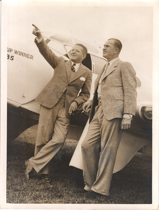 Two men in suits posing beside an airplane in a vintage black and white photograph. - Image: Folder28-13