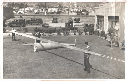 Vintage black-and-white photograph of young men with a glider model and classic cars in the background. - Image: Folder3-5