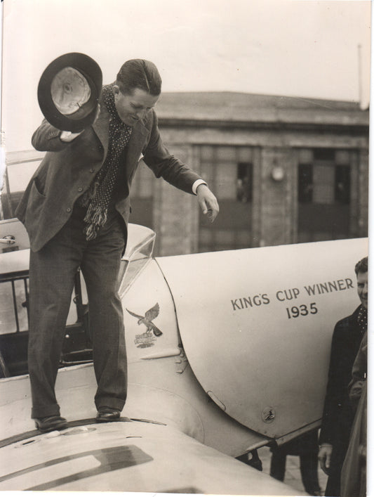 A vintage photograph of a pilot celebrating on an airplane, labeled "King's Cup Winner 1935." - Image: Folder28-11